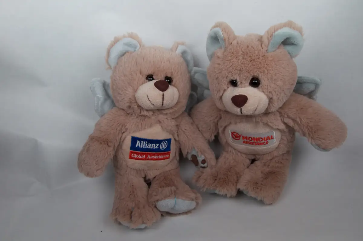 Derselbe Schutzbär in zwei Markenständen: links mit Aufnäher Allianz Global Assistance, rechts mit Mondial Assistance